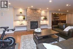Fireplace with stone surround, recessed lighting, built-in shelving with accent lighting, wood-finish flooring, and a dedicated wet bar area - 