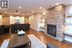 Stone-clad fireplace with built-in insert, wood-finish flooring, recessed lighting, built-in shelving with accent lighting, and a projector screen - 