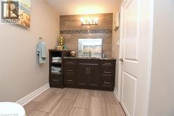 Wood-finish tile flooring, espresso wood vanity with integrated storage, counter-mounted sink, and tiled backsplash with decorative accent - 
