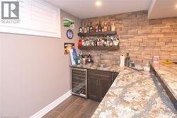 Wet bar featuring stone accent wall, wood-finish flooring, recessed lighting, built-in wine refrigerator, and a stainless steel sink - 