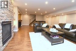 Stacked stone fireplace surround, wood-finish flooring, recessed lighting, and a finished staircase with wood railing - 