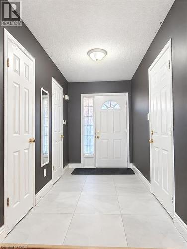 Entryway featuring large-format light tile flooring, white six-panel interior doors, and a front entry door with a decorative glass sidelight and transom window - 52 Isabella Street, Kitchener, ON 