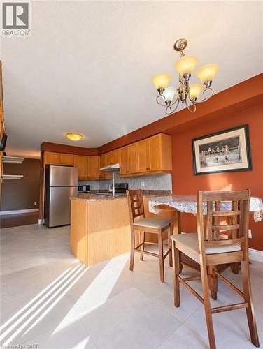 Kitchen featuring natural wood cabinetry, stone-finish countertops, stainless steel refrigerator, tile flooring, and a five-light chandelier - 52 Isabella Street, Kitchener, ON 