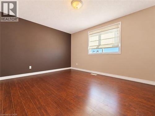 Room featuring wood-finish flooring, a deep brown accent wall, a single window with integrated blinds, and a central ceiling light fixture - 52 Isabella Street, Kitchener, ON 