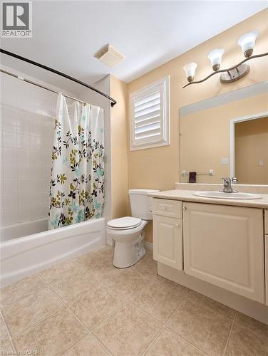 Bathroom featuring a white vanity cabinet with a composite countertop, integrated sink basin, large wall-mounted mirror, three-light fixture, and ceramic tile flooring - 52 Isabella Street, Kitchener, ON 