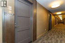 Entry door featuring wood-veneer trim, satin nickel hardware, and a modern unit number plate, complemented by textile-textured wall coverings and recessed oval ceiling lighting - 