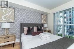 Bedroom featuring patterned accent wall, wood-finish flooring, and floor-to-ceiling glass paneling with sliding door access to an exterior balcony - 