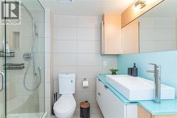 Bathroom featuring a glass-enclosed shower with a rainfall showerhead, a rectangular vessel sink on a custom vanity, a glass backsplash, and neutral large-format wall tile - 