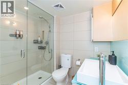 Walk-in shower with frameless glass enclosure, wall-mounted handheld shower fixture, built-in recessed niche, light-finish cabinetry, and rectangular vessel sink with chrome hardware - 