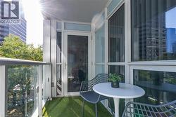 Private balcony with synthetic turf flooring, glass panel railings, and floor-to-ceiling glass-paneled entry door - 
