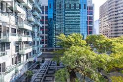 Modern high-rise exterior featuring glass-railing balconies, patterned stone paver courtyard, and mature deciduous trees - 