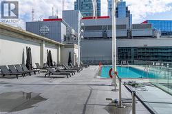 Rooftop terrace featuring a rectangular swimming pool, expansive stone-tiled decking, and glass panel railing - 