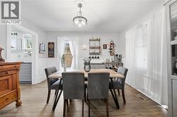 Dining area featuring wood-finish flooring, white wainscoting, a multi-bulb pendant light fixture, and large windows with integrated blinds - 
