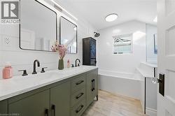 Dual-sink vanity with stone-finish countertop, matte black fixtures, shiplap wall detailing, wood-finish flooring, and built-in soaking tub - 