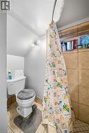 Bathroom featuring square ceramic wall tiles, tiled floor, a shower area, and a dual-bulb wall-mounted light fixture - 