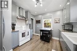 Kitchen featuring shaker-style cabinetry, white apron-front sink, stainless steel range hood, stone countertops, and wood-finish flooring - 