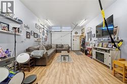 Enclosed garage space featuring wood-finish flooring, dual linear overhead light fixtures, a white roll-up garage door, and a dedicated entry door - 