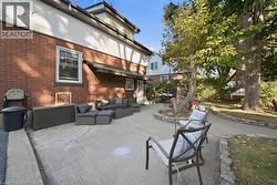 Rear exterior featuring a brick facade, concrete patio, stone-lined landscape edging, and mature trees - 
