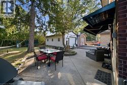 Expansive concrete patio featuring a retractable awning, stone-bordered landscaping, mature trees, and a detached garage - 