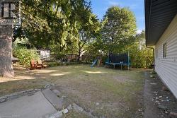 Backyard featuring mature trees, horizontal siding, stone-bordered concrete hardscaping, and wooden perimeter fencing - 