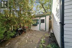 Detached storage structure featuring white horizontal siding, green trim, and an integrated window box, complemented by flagstone hardscaping and mature evergreen screening - 
