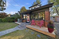 Exterior facade featuring red brick masonry, a wood-plank deck, curved concrete entry steps, large window expanses, and a prominent glass-panel front door - 