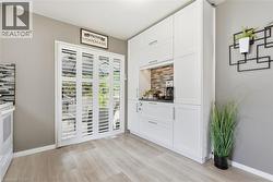 White cabinetry with integrated appliances, wood-finish flooring, and a stone-tiled backsplash - 