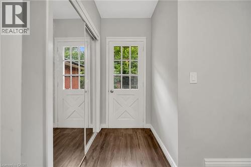 Wood-finish flooring, white paneled doors with clear glass panes, and mirrored sliding closet doors - 284 Cedar Crescent, Cambridge, ON - Indoor Photo Showing Other Room