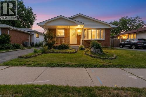 Brick and siding bungalow featuring a covered front porch with white railing, a concrete driveway, and a manicured lawn with decorative rock accents - 1259 Ernest Avenue, London, ON - Outdoor
