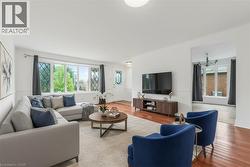 Bright living area featuring wood-finish flooring, white walls, and a large front window with decorative grilles - 