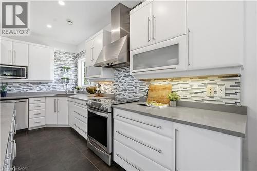 White cabinetry with sleek hardware, stainless steel appliances, gray countertops, and a full-height tile backsplash with under-cabinet lighting - 5779 Third Line, Guelph/Eramosa, ON - Indoor Photo Showing Kitchen With Upgraded Kitchen