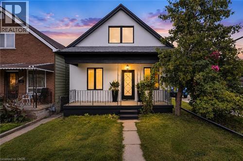 Gabled roofline, front porch with black railing, black front door with decorative glass, white exterior siding, and black trim windows - 174 London Street N, Hamilton, ON - Outdoor With Deck Patio Veranda