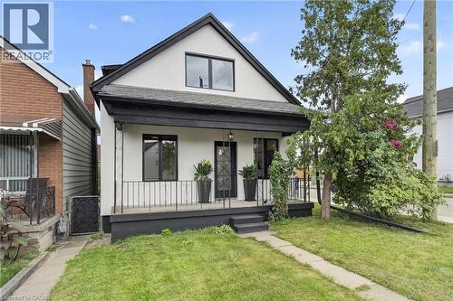 Gable roofline, white exterior siding, black trim accents, covered porch with black railings, and a mature tree - 174 London Street N, Hamilton, ON - Outdoor With Deck Patio Veranda