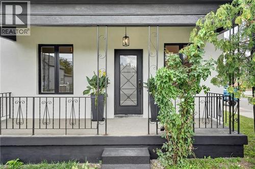 Covered porch with wrought iron railings, dark frame windows, an ornate front door, and a suspended exterior light fixture - 174 London Street N, Hamilton, ON - Outdoor With Deck Patio Veranda