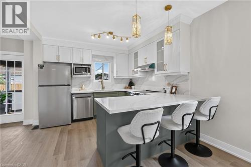 Kitchen featuring stainless steel appliances, white shaker cabinetry, a large center island with seating, pendant lighting, and wood-finish flooring - 174 London Street N, Hamilton, ON - Indoor Photo Showing Kitchen With Stainless Steel Kitchen With Upgraded Kitchen