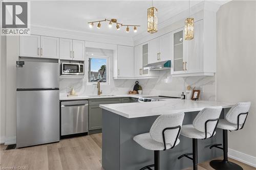 Kitchen featuring stainless steel appliances, white cabinetry, a kitchen island with a white countertop, and wood-finish flooring - 174 London Street N, Hamilton, ON - Indoor Photo Showing Kitchen With Upgraded Kitchen