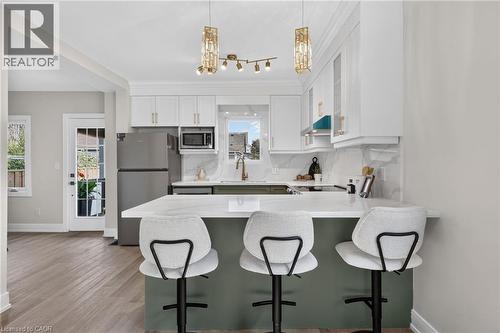 Kitchen featuring white upper cabinetry, a green lower cabinet island, light-toned wood-finish flooring, and a stainless steel refrigerator - 174 London Street N, Hamilton, ON - Indoor Photo Showing Kitchen With Double Sink With Upgraded Kitchen