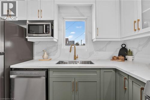 White upper cabinetry with gold-tone hardware, contrasting sage lower cabinetry, stainless steel dishwasher, undermount stainless steel sink with gold-tone faucet, and white countertops with a marble- - 174 London Street N, Hamilton, ON - Indoor Photo Showing Kitchen With Stainless Steel Kitchen With Double Sink With Upgraded Kitchen