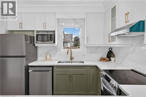 Kitchen featuring stainless steel appliances, white upper cabinetry, olive-toned lower cabinetry, white countertops, and a dual basin sink with a gold-tone faucet - 174 London Street N, Hamilton, ON - Indoor