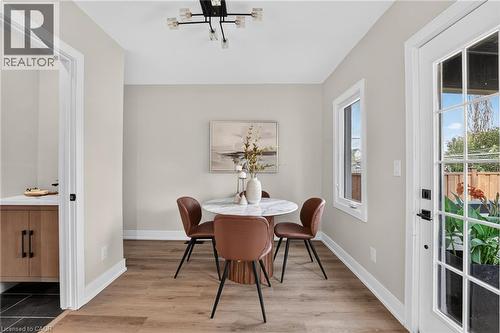 Wood-finish flooring, contemporary ceiling light fixture, white window trim, white baseboards, and a glass-paneled exterior door - 174 London Street N, Hamilton, ON - Indoor Photo Showing Dining Room