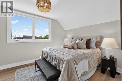 Recessed wall with a large window, light-toned walls, wood-finish flooring, and a contemporary ceiling light fixture - 174 London Street N, Hamilton, ON - Indoor Photo Showing Bedroom