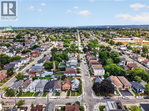 Established neighborhood with a mix of residential properties, mature tree canopy, paved streets, and visible commercial buildings in the distance - 174 London Street N, Hamilton, ON - Outdoor With View