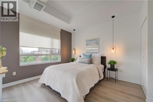 Spacious room featuring wood-finish flooring, a large window with roller shades, and two distinct pendant light fixtures - 191 King Street S Unit# 607, Waterloo, ON - Indoor Photo Showing Bedroom