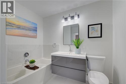 Bathroom featuring a floating vanity with a integrated sink, a rectangular mirror, a three-light fixture, a built-in bathtub with tile surround, and a toilet - 191 King Street S Unit# 607, Waterloo, ON - Indoor Photo Showing Bathroom