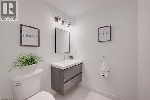 Bathroom featuring a floating vanity with integrated sink, a rectangular mirror, a three-light fixture with clear glass shades, a ceramic toilet, and large format floor tiles - 191 King Street S Unit# 607, Waterloo, ON - Indoor Photo Showing Bathroom