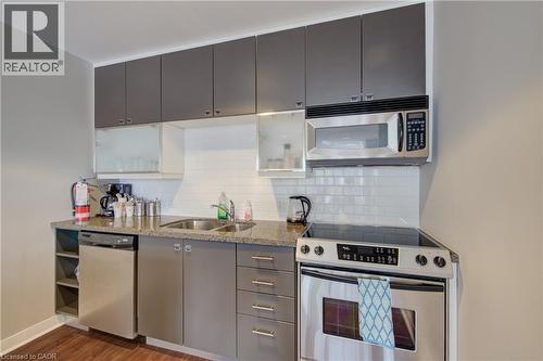 Building  Party Room Compact kitchen featuring wood-finish flooring, grey cabinetry, a stainless steel dishwasher, a stainless steel electric range, and a built-in stainless steel microwave - 191 King Street S Unit# 607, Waterloo, ON - Indoor Photo Showing Kitchen With Stainless Steel Kitchen With Double Sink