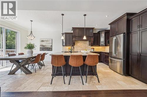 Open-concept kitchen and dining area featuring dark wood cabinetry, stainless steel appliances, a center island with countertop seating, and stone tile flooring. - 828 Copper Ridge Drive, Waterloo, ON - Indoor
