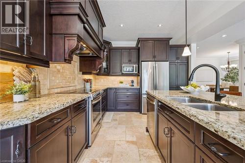 Gourmet kitchen featuring rich wood cabinetry, stainless steel appliances, stone slab countertops, a tile backsplash, and recessed lighting - 828 Copper Ridge Drive, Waterloo, ON - Indoor Photo Showing Kitchen With Double Sink With Upgraded Kitchen