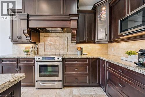 Kitchen featuring rich wood cabinetry, stone countertops, a tile backsplash, and stainless steel appliances including a range and microwave. - 828 Copper Ridge Drive, Waterloo, ON - Indoor Photo Showing Kitchen With Upgraded Kitchen