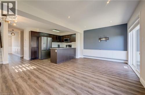 Open-concept living space featuring wood-finish flooring, a contemporary kitchen with stainless steel appliances, a kitchen island, and dark cabinetry - 80 Miranda Path, Elmira, ON - Indoor Photo Showing Kitchen